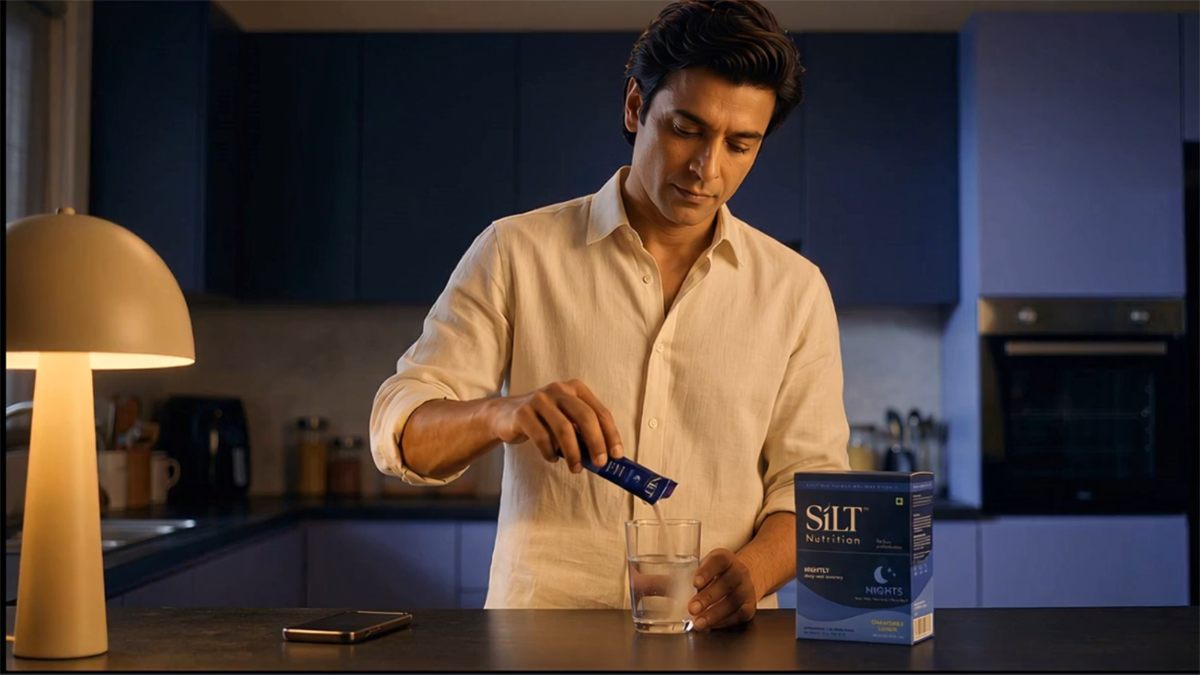 A man pours a SILT Nights stick into a glass of water at a kitchen counter, box beside him.